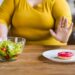 Pensive fat chubby obese caucasian woman opting for healthy food instead of sweets. Dieting concept. Hard choice between healthy lifestyle and bad eating habits.
