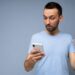 Handsome brunet man wearing everyday clothes isolated on blue background wall with copy space holding and using mobile phone and plastic credit card making payment.