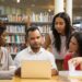 Concentrated young people reading information from laptop. Cheerful students working with laptop at library. Education concept