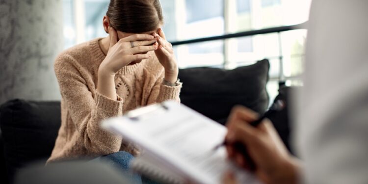 Sad woman holding her head in pain while having a meeting with psychotherapist.
