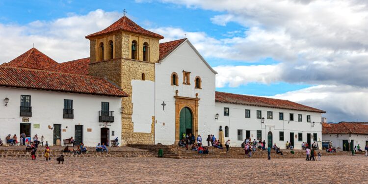 Villa de Leyva, Colombia - The church on the Plaza Mayor of the historic 16th Century town of Villa de Leyva. Founded in 1572 and located at an altitude of just over 7000 feet above mean sea level on the Andes Mountains, Villa de Leyva was declared a National Monument by the Colombian Government in 1954 to protect its colonial architecture and heritage. It is located in the Department of Boyacá. The square is the largest town square in Colombia. Colombians visiting the town and local residents are seen on the square just sitting and relaxing, chatting with friends or going about their routine chores. In the background are the Andes Mountains. The Town was one of the locations for the movie Cobra Verde by Werner Herzog and the Spanish language Soap Opera Zorro. Photo shot in the afternoon sunlight; horizontal format. Copy space.
