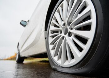 Close up view on stopped white car with punctured car tire on a road. Focus on a wheel.