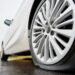 Close up view on stopped white car with punctured car tire on a road. Focus on a wheel.