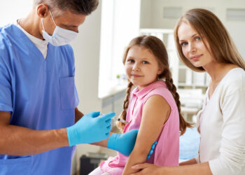 Smiling girl looking at camera while doctor making her an injection in clinics