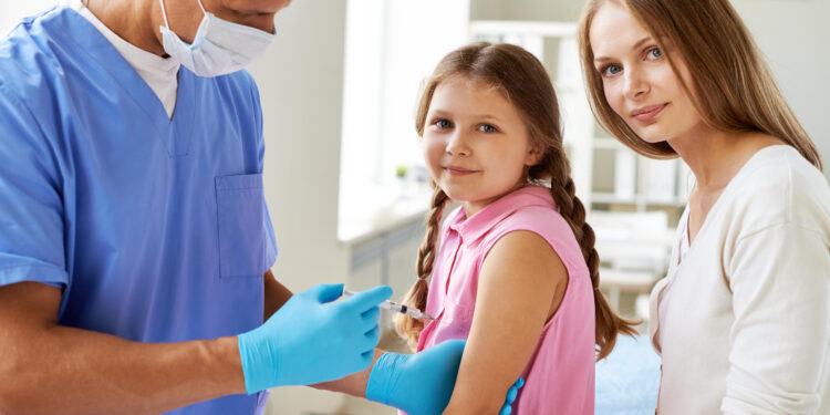 Smiling girl looking at camera while doctor making her an injection in clinics