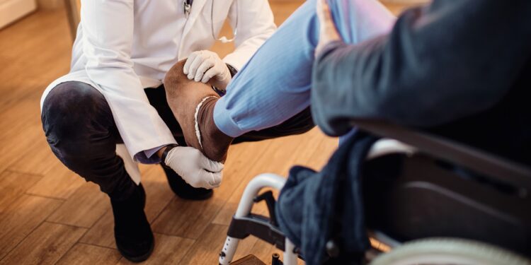 Unrecognizable senior man in wheelchair getting his leg examined by a doctor at nursing home.