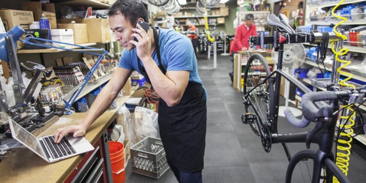 Technician using cell phone and laptop in bicycle repair shop