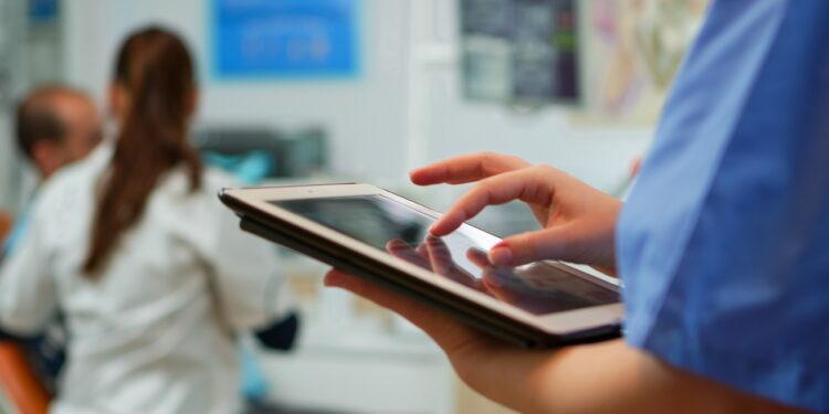 Close up of nurse holding and typing on tablet standing in stomatologic clinic, while doctor is working with patient in background. Using monitor with chroma key izolated pc key mockup pc display