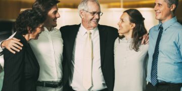 Closeup of smiling senior business man embracing colleagues. They are standing and with blurred view in background.