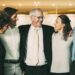 Closeup of smiling senior business man embracing colleagues. They are standing and with blurred view in background.