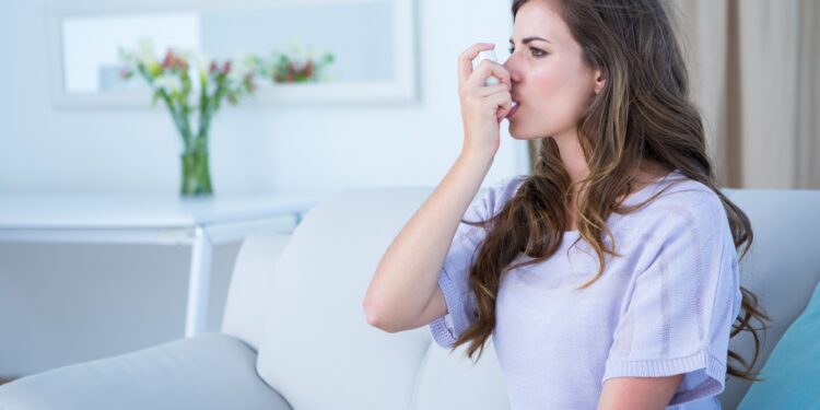 Pretty woman taking her inhaler at home at the living room