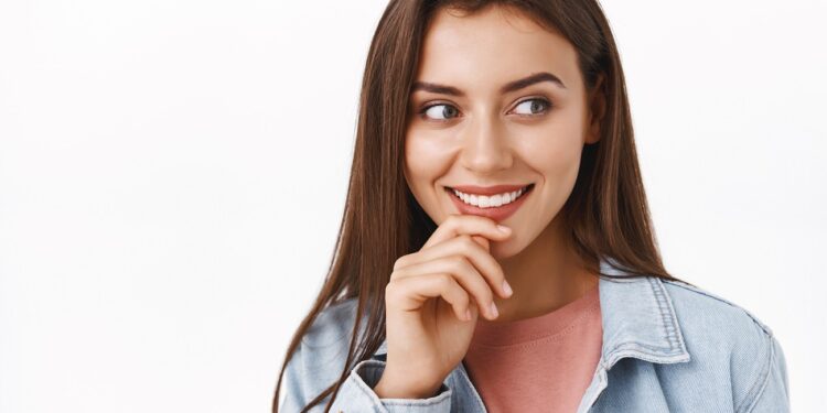 Curious and intrigued alluring modern woman in denim jacket, look at something tempting and entertaining, touch lip thoughtful, smiling, beaming from interest, stand white background.