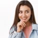Curious and intrigued alluring modern woman in denim jacket, look at something tempting and entertaining, touch lip thoughtful, smiling, beaming from interest, stand white background.