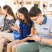 Young boy with friends using smart phones sitting on bench outdoors