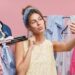Pretty young female making selfie while standing near racks with clothes, being glad to spend her free time in shopping centre. Adorable lady using modern mobile phone while doing shopping alone.