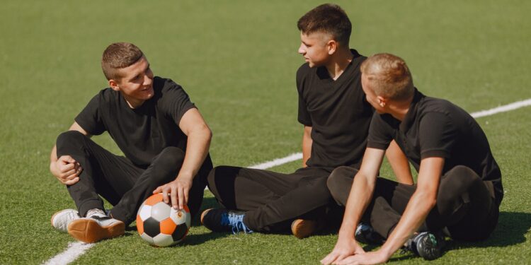 Men play socer at the park. Tournament on mini-footbal. Guy in a black sportsuits.