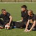 Men play socer at the park. Tournament on mini-footbal. Guy in a black sportsuits.