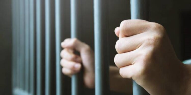 Man in prison hands of behind hold Steel cage jail bars. offender criminal locked in jail.