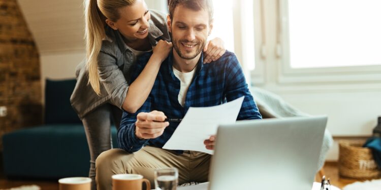 Happy couple analyzing their home budget while paying bill on a computer.