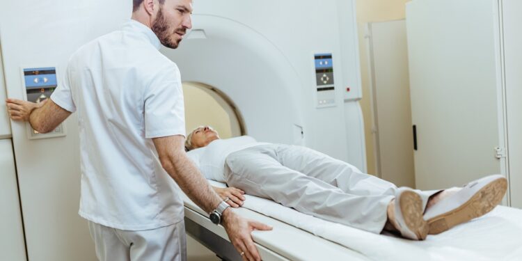 Medical technician starting MRI scanning examination of a female patient at medical clinic.