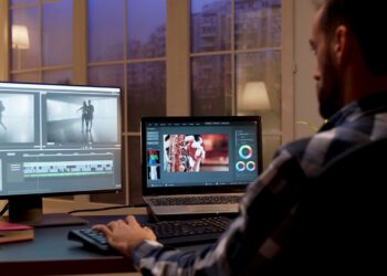 Back view of content creator working in home office during night time. Video editor in home office.