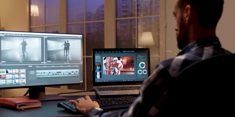 Back view of content creator working in home office during night time. Video editor in home office.