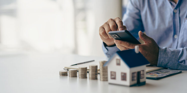 House of piles of coins in front notebook and pen Young man writing by hand. Prepare a plan. Saving coins to buy a house as real estate.