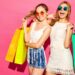 Portrait of two young stylish smiling blond women holding shopping bags. Girls dressed in summer hipster clothes. Positive models posing over pink blackground