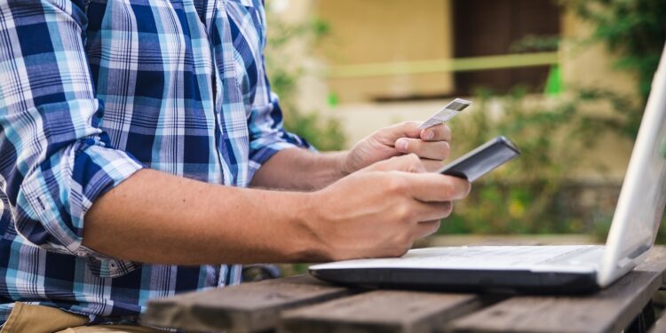 Handsome man relaxing in his garden using laptop to shop on a sunny day