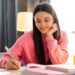 Young girl, teenager sitting at her desk at home, taking notes from a textbook. She smiling and appears to be enjoying her studies. Homework, education concept