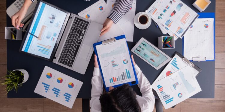 Top viewTop view of manager and employee doing teamwork in business office , looking at charts on laptop display. Finance paperwork with charts at workplace. Discusing financial plan.