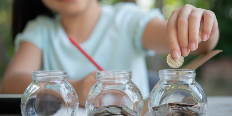 Cute asian little girl playing with coins making stacks of money,kid saving money into piggy bank, into glass jar. Child counting his saved coins, Children learning about for the future concept.