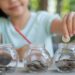 Cute asian little girl playing with coins making stacks of money,kid saving money into piggy bank, into glass jar. Child counting his saved coins, Children learning about for the future concept.
