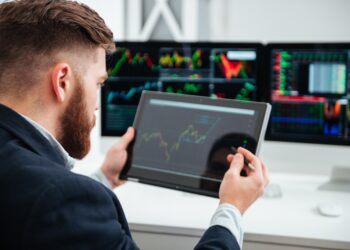 Back view of bearded young businessman sitting and woking with tablet in office