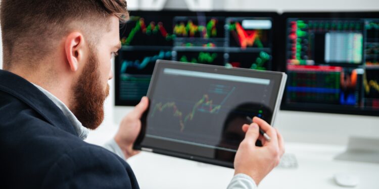 Back view of bearded young businessman sitting and woking with tablet in office