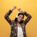 Joyful woman in white top, stylish brown jacket smiles and dances on yellow background. Attractive girl listening to music in headphones on isolated.