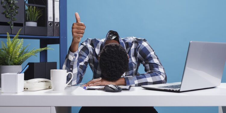 Extremely fatigued office person suffering from burnout syndrome showing thumbs up to coworkers for doing a good job. Exhausted businessman falling asleep because of overwork while showing OK symbol.