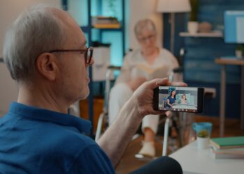 Retired man talking to daughter and niece in hospital on video call, sitting next to crutches. Person using smartphone to chat on online videoconference with relatives at health clinic.