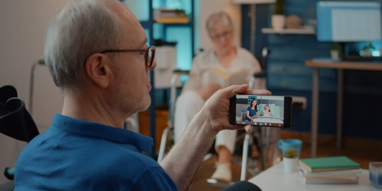 Retired man talking to daughter and niece in hospital on video call, sitting next to crutches. Person using smartphone to chat on online videoconference with relatives at health clinic.