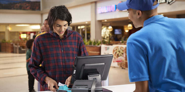 Young man paying for movie tickets at checkout counter in cinema hall