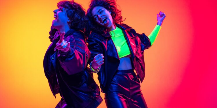 Portrait of young emotive people, man and woman wearing leather cloth, dancing isolated over gradient background in neon