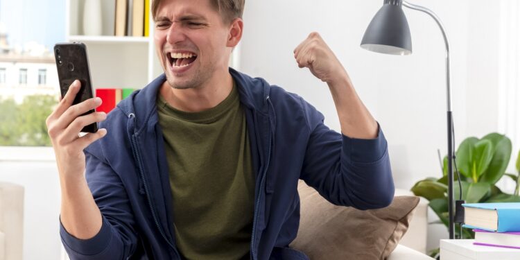 excited young blonde handsome man sits on armchair keeping fist and looking at phone inside design living room SSUCv3H4sIAAAAAAAACpyRz27DIAzG75P2DhHnRiIk6p+9SrWDY1iDSqECsmmq+u4zECrOu+Gf7c/+zOP9revYDEEj++geKaJYG7OG6CFqZwnz3ca9slL5liipo/MaTAtniLhYuCmCdjUm4WdOshAhrkGFNGxDCFFdSKPAl0TZ6FziriZykjooxdiuYWGdM6uoiP+rszw+qxu4KIu/eeHGiFdGQTFyLqXs+hOVv7XWYJXaNa6+HYJJBWOjdPcatb00bS4u+cq1Dd1qo08rvDZnxrk7zCad+Is0VeULhEDlsvJmENKfulszx7qYDWyqTNJPpHAYxXSahOCcH04DHw77raD83qJJJ69ThSjGq5atdZ02YHwa4XQUop+PQvWTlKqfBQ69ADwgiiMXsKfDP/8AAAD//wMALedqr4cCAAA=