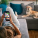 Young woman resting in her apartment on the sofa together with her Labrador retriever dog and ordering food for lunch online. She is holding a mobile phone and choosing meal to buy from the menu on the website. Photos used for app interface is my own photos, also available in my portfolio with photo IDs: 182682315, 182675346, 182702479