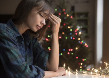 Mixed Race woman with headache near Christmas tree
