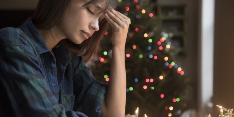 Mixed Race woman with headache near Christmas tree