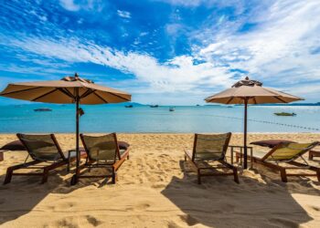 Beautiful tropical beach sea and ocean with coconut palm tree  and umbrella and chair on blue sky and white cloud for holiday vacation travel