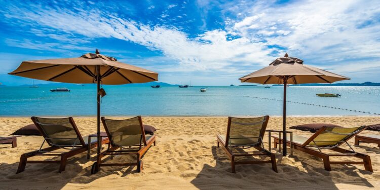 Beautiful tropical beach sea and ocean with coconut palm tree and umbrella and chair on blue sky and white cloud for holiday vacation travel