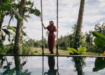 Photo from back of slim woman in long dress looking at rainy sky. Outdoor shot of shapely female model enjoying nature views at resort.
