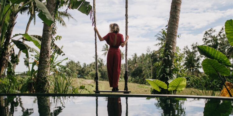 Photo from back of slim woman in long dress looking at rainy sky. Outdoor shot of shapely female model enjoying nature views at resort.
