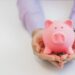 Businessman in a suit holding pink piggy bank with both hands, isolated on white background.